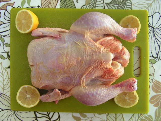 whole chicken on a green board with lemons