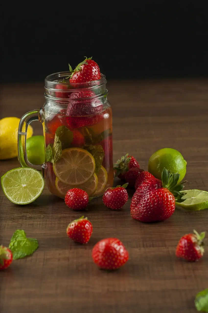 A glass mason jar with strawberries and limes infusing in water